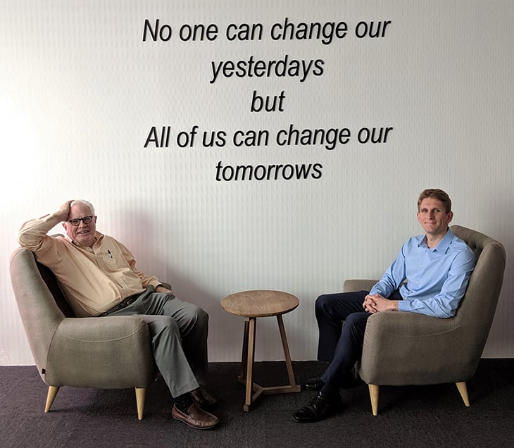 Two men sitting with a motivational quote on the wall