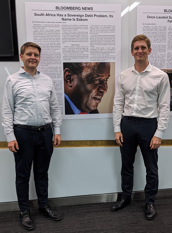 Two men standing in front of a large news article page