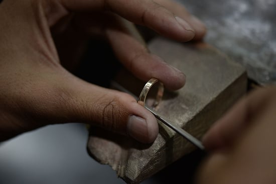 A craftsman polishing a gold jewelry piece to precise measurements.