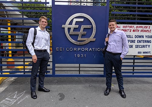 Two men posing next to a EEI Corporation gate sign