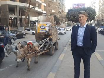 A man in a suit standing next to a donkey pulled cart